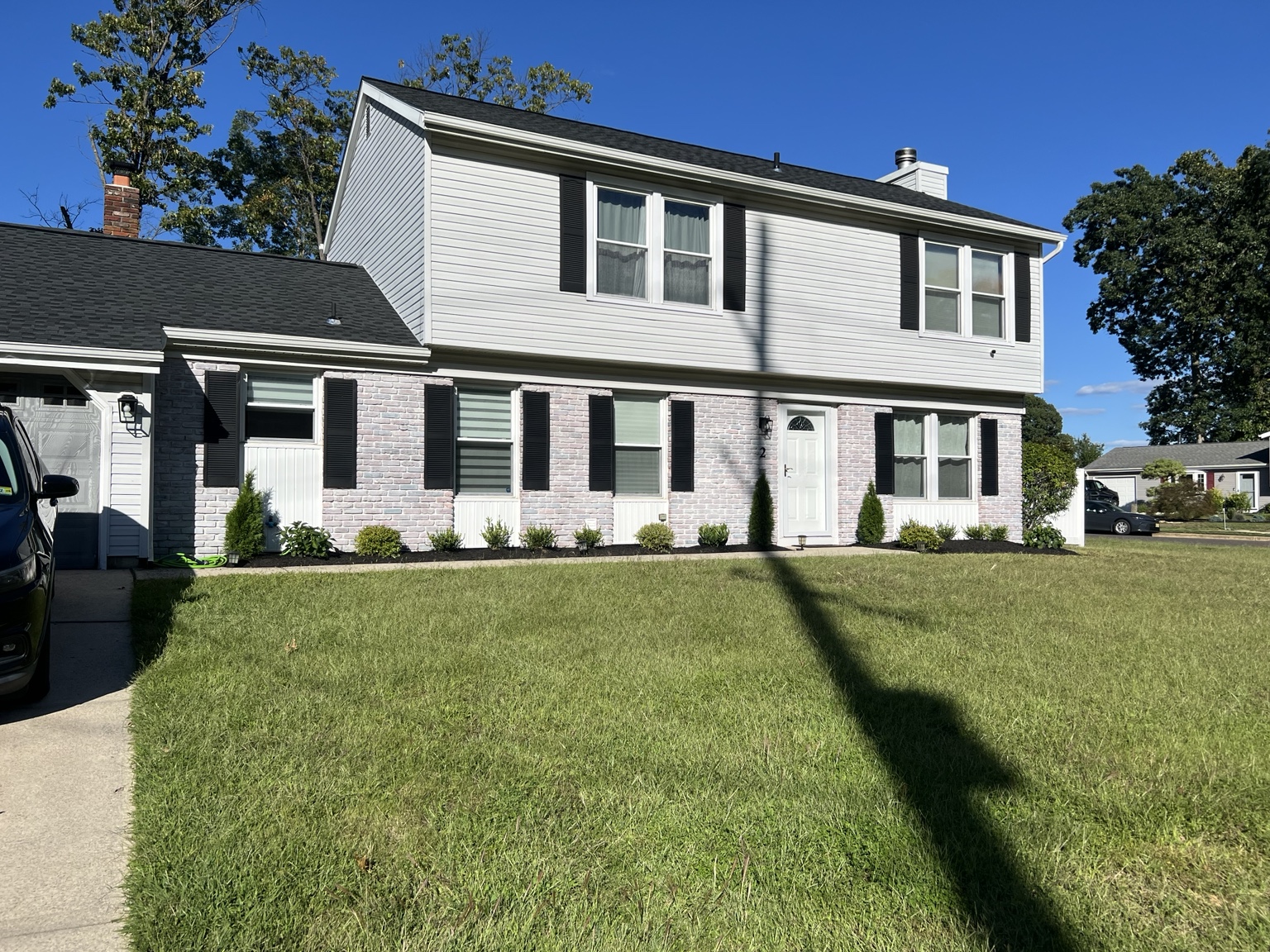 Completed exterior home refresh with white brick, black shutters, and fresh landscaping